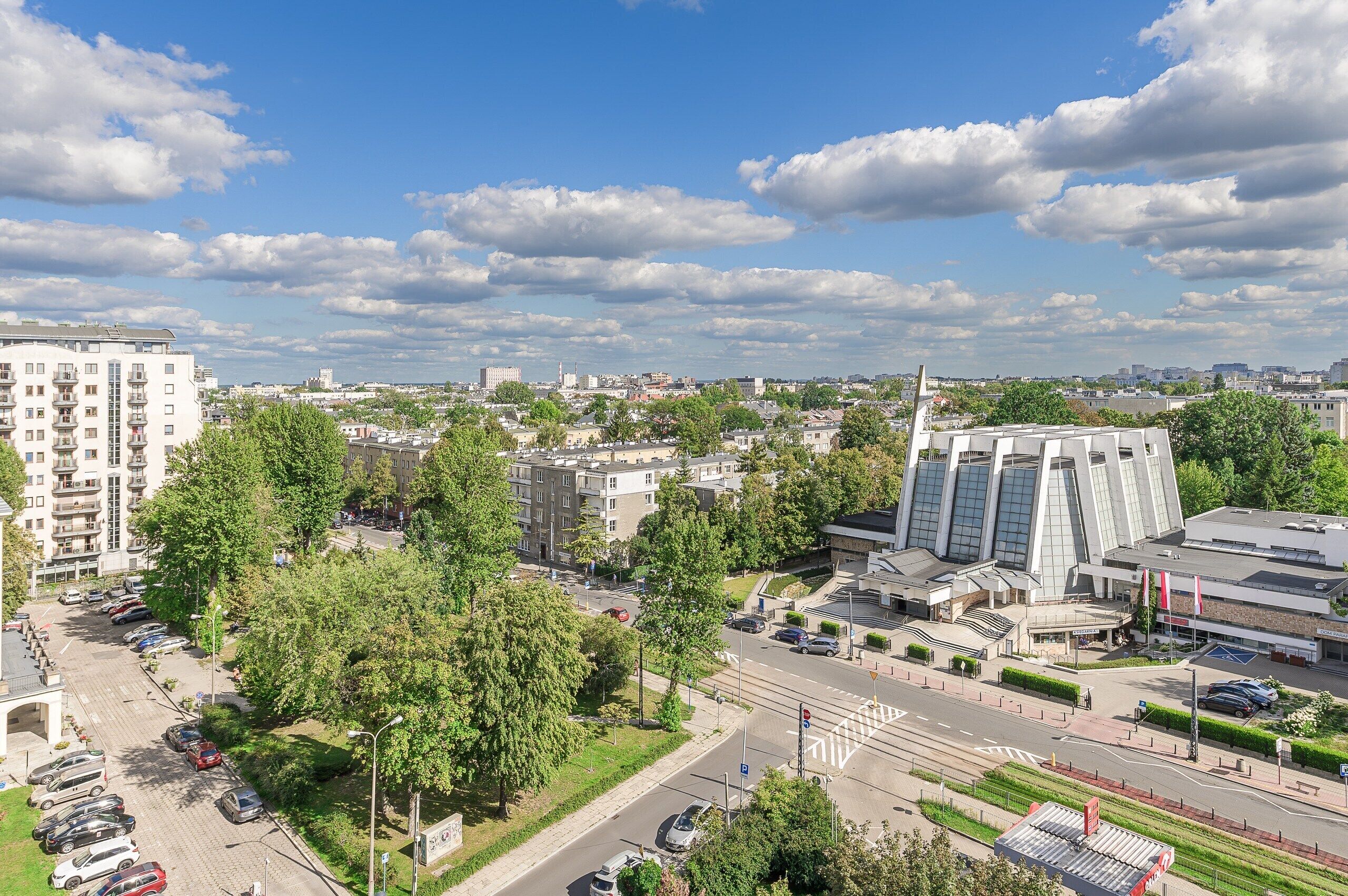Eine Stadtansicht mit einer Mischung aus Wohn- und Geschäftsgebäuden, einem Parkplatz und blauem Himmel.