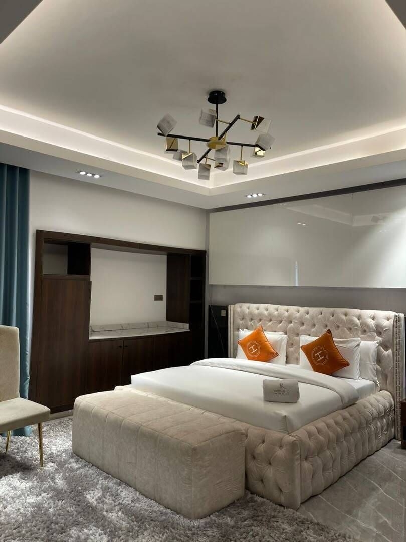A modern bedroom with a large bed, a built-in TV, and a unique ceiling light fixture.