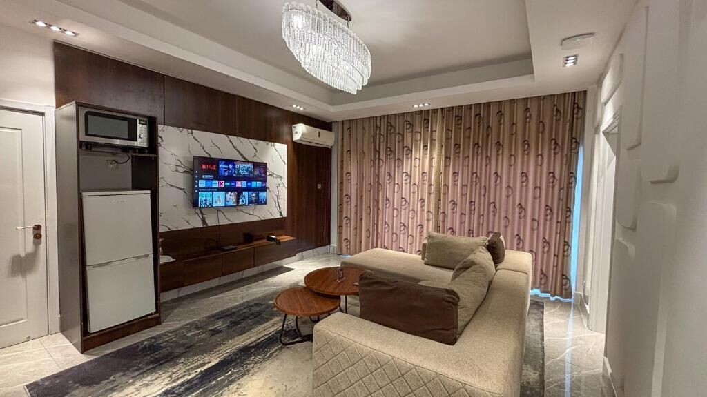 Un salon moderne avec un canapé, une table basse, un téléviseur fixé sur un mur en marbre et un rideau à motifs.