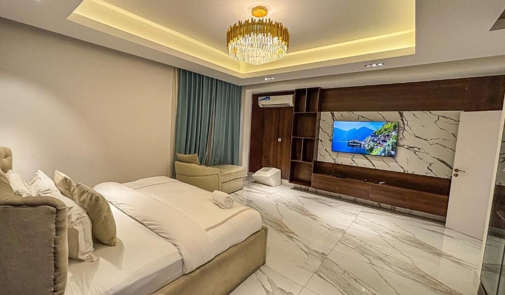 A modern bedroom with a large bed, a TV mounted on a marble wall, and a chandelier.