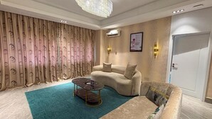 A living room with a curved sofa, a small coffee table, and a chandelier. - Mac Residence (Lagos)