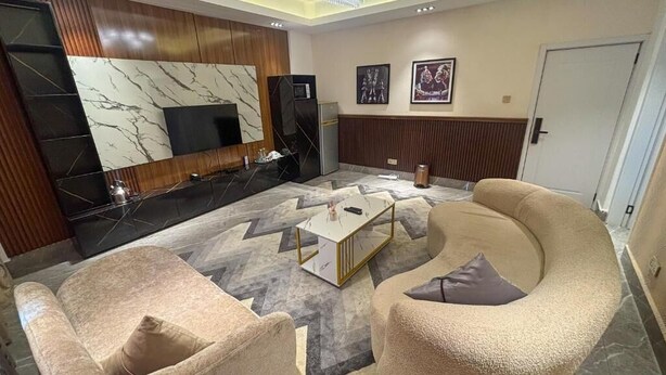 A modern living room with a sofa, armchairs, a coffee table, and a flat-screen TV mounted on a wall with a marble design. - Mac Residence (Lagos)