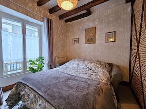 Un dormitorio con una cama, un radiador, una ventana con cortinas y una planta.