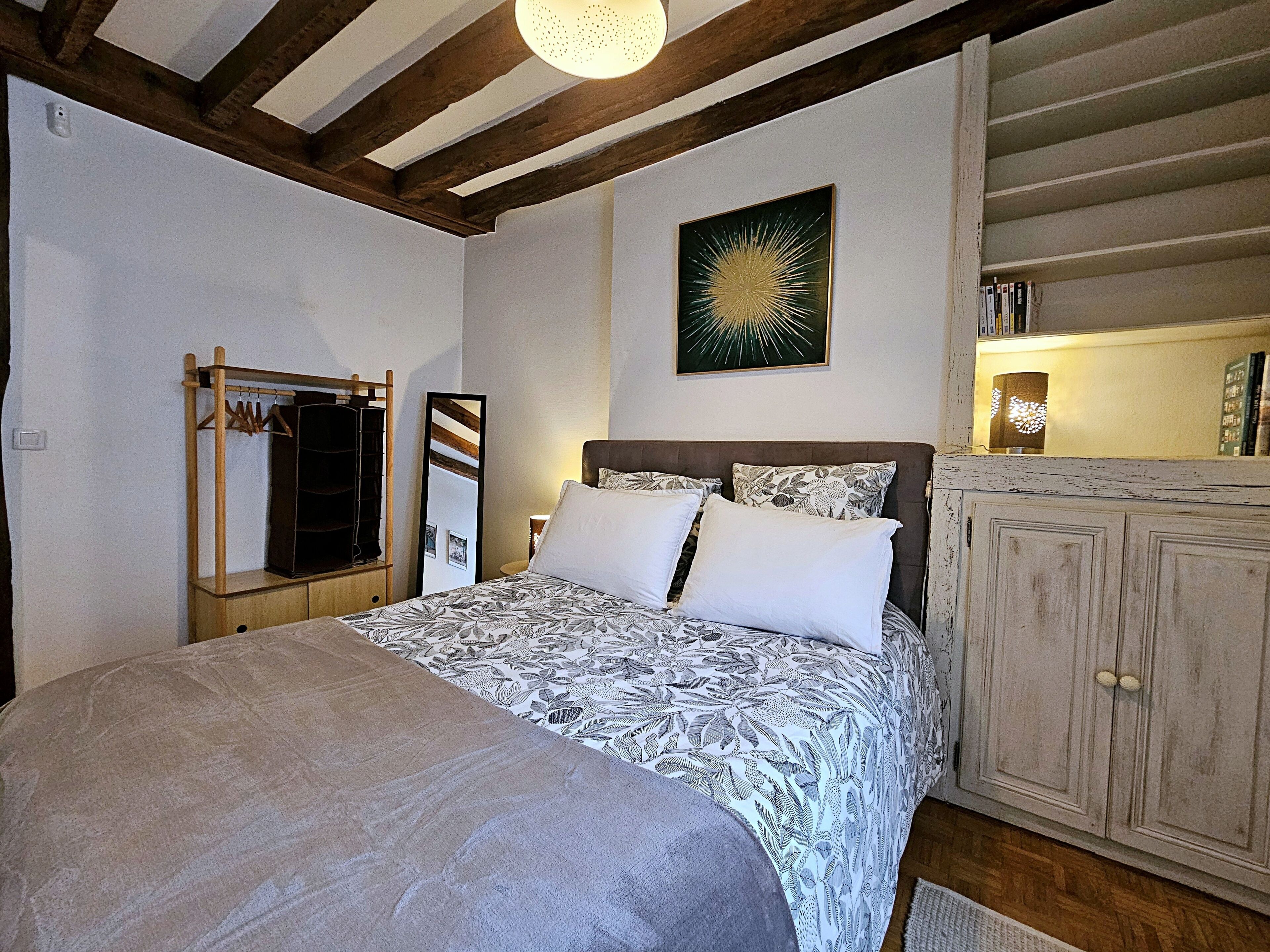 Een slaapkamer met een bed, een kledingkast, een spiegel en een kunstwerk aan de muur.