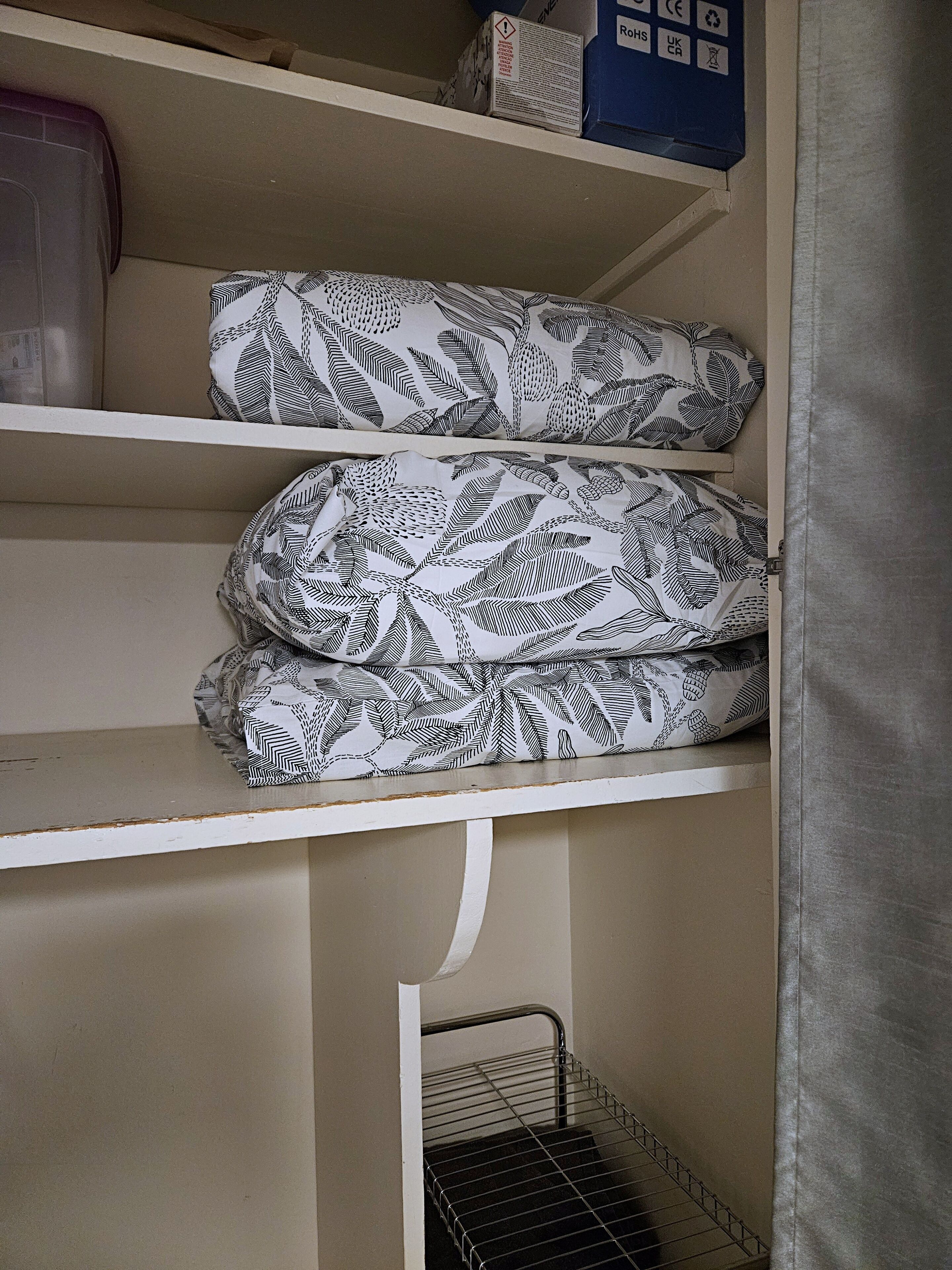 A storage area with shelves holding patterned fabric items and a metal rack below.