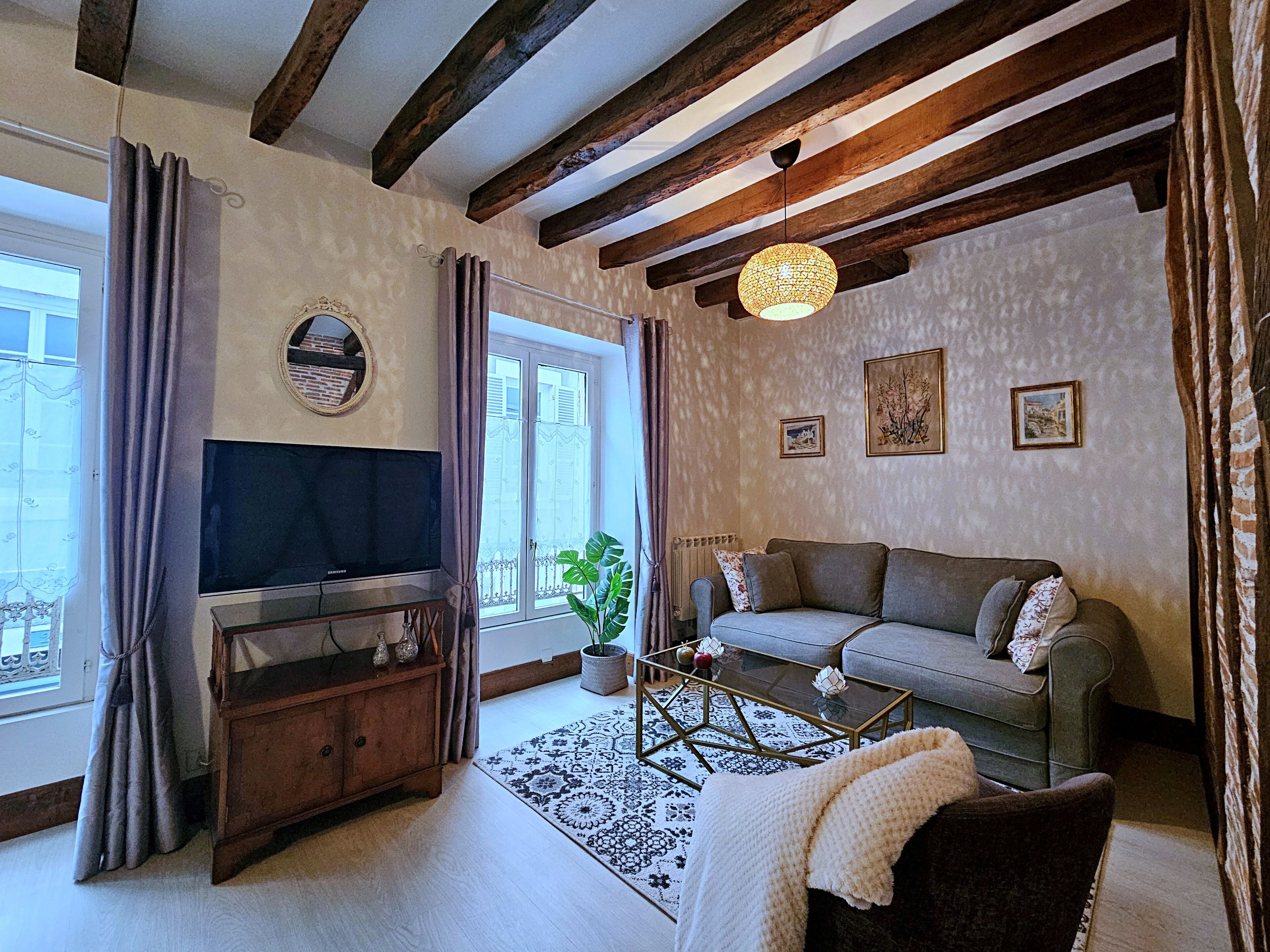 Un salon avec un canapé, un téléviseur, une table basse en bois et un tapis à motifs.