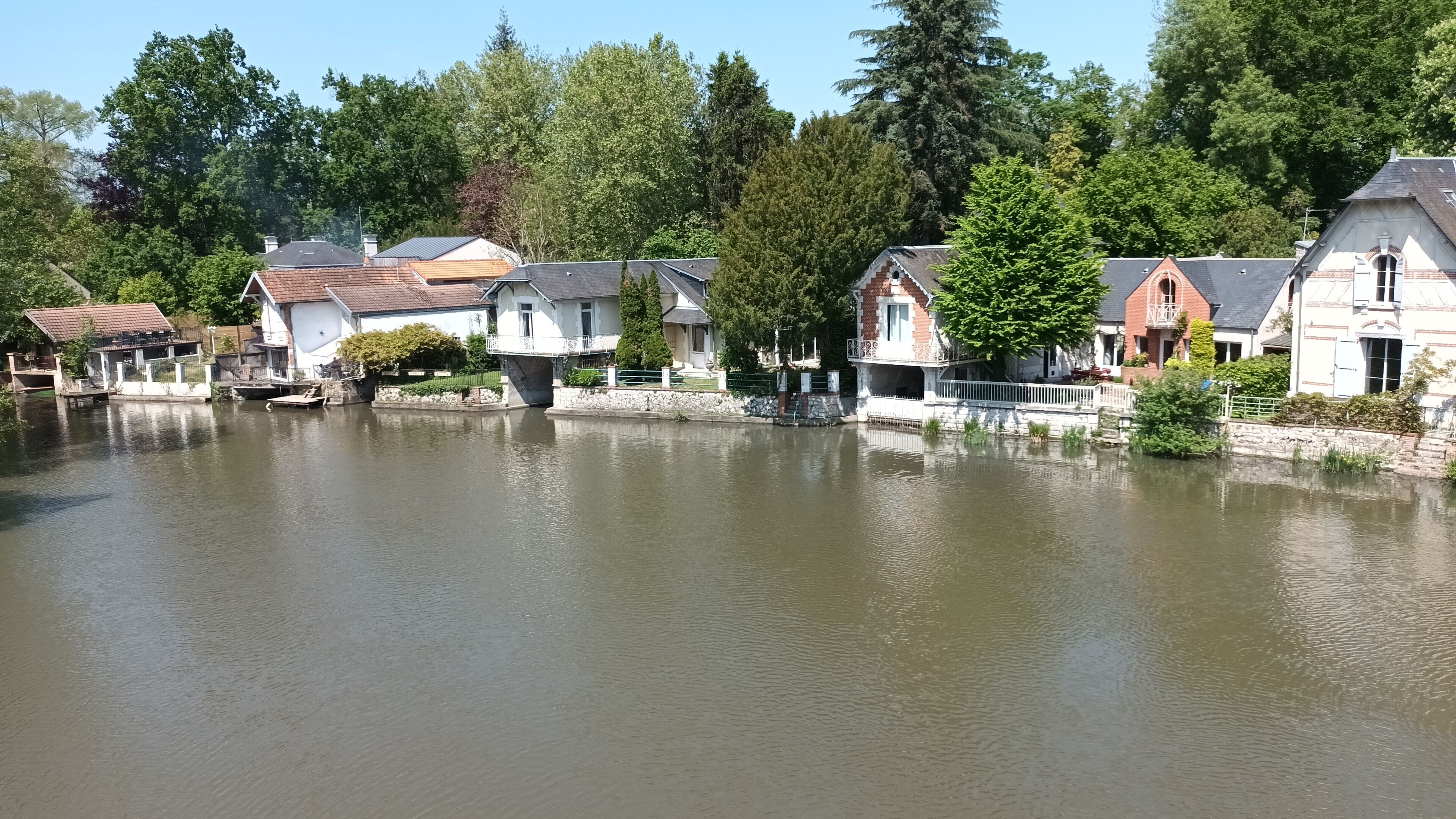 Un quartier résidentiel au bord d’un lac, avec des maisons construites le long du rivage, des allées pavées et une végétation luxuriante.