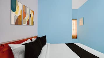 A hotel room with a bed, a headboard, a wall-mounted light fixture, and three abstract paintings.
