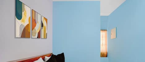 A hotel room with a bed, a headboard, a wall-mounted light fixture, and three abstract paintings.