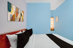 Habitación de hotel con cama, cabecera, lámpara de pared y tres cuadros abstractos.