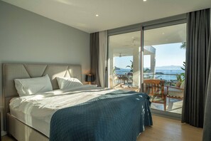 Ein Schlafzimmer mit einem großen Bett, einem Balkon mit Tisch und Stühlen und Blick aufs Meer.