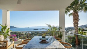 A balcony with a marble table, wooden chairs, and a view of the sea and distant mountains. - Villa Matie Bodrum Views (Bodrum)