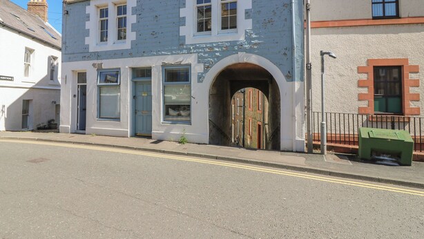 A two-story building with a blue facade, a central arched doorway, and a street view. - The Herring's Lean (Eyemouth)