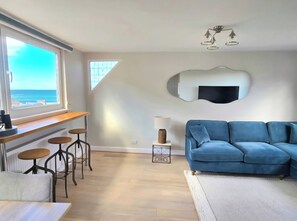 Een moderne woonkamer met een blauwe bank, een houten bar en barkrukken.