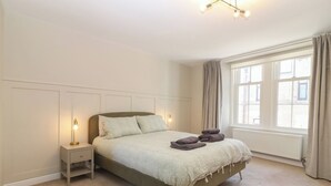A bedroom with a bed, nightstands, a window with curtains, and a radiator. - The Herring's Lean (Eyemouth)