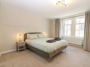 Ein Schlafzimmer mit Bett, Nachttischen, einem Fenster mit Vorhängen und einer Heizung.