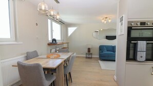 A modern kitchen with a dining area, a blue sofa, and a view of the living room. - The Herring's Lean (Eyemouth)