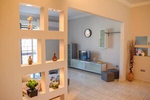 A modern living room with a television, a sofa, and a coffee table. There is a large window providing natural light and a view of the outdoors. - Cozy flat on the main square, 10min to the sea (Kalamata)