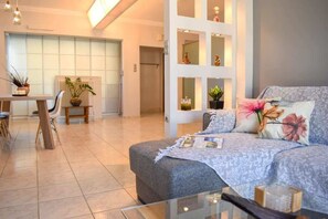 A modern living room with a sofa, a glass coffee table, and a dining area with a table and chairs. - Cozy flat on the main square, 10min to the sea (Kalamata)
