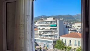 Blick aus dem Fenster auf ein mehrstöckiges Gebäude mit Balkonen, einem klaren Himmel und entfernte Berge.