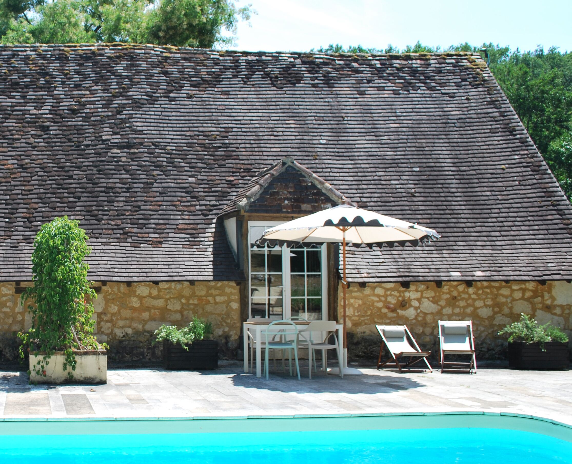 A stone building with a sloped roof, a pool, and outdoor seating.