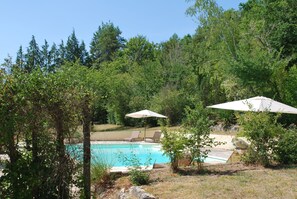 Ein Swimmingpool, umgeben von Bäumen und zwei Liegestühlen mit Sonnenschirmen.