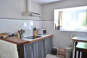 A kitchen with a stove, microwave, and a window with curtains. - Gîte du verger avec piscine dans un domaine périgourdin (Saint-Georges-de-Montclard)