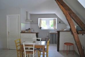Une cuisine avec une table à manger, des chaises, une fenêtre et une structure en poutres apparentes.