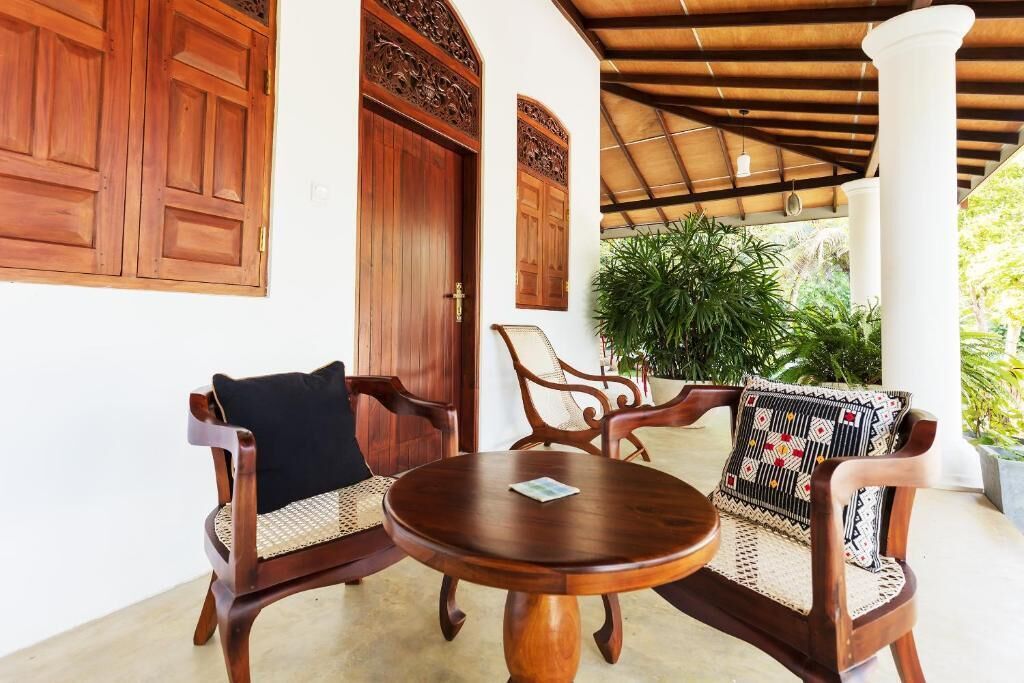 Une table en bois avec deux chaises, une grande porte en bois et un espace abrité avec des colonnes.
