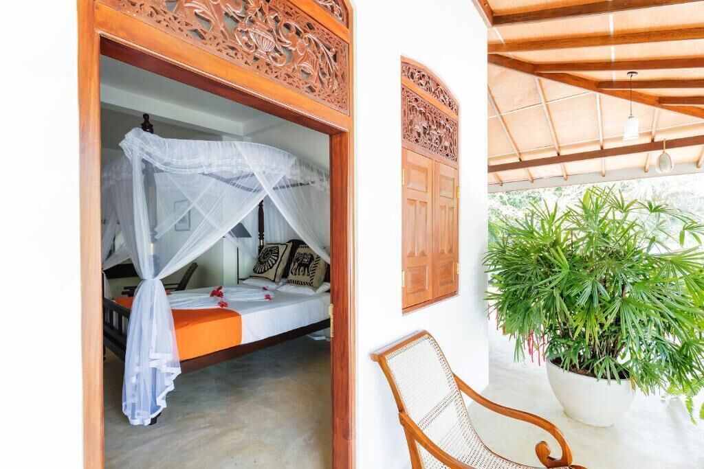 Una habitación con una cama bajo un dosel, una silla y una planta en maceta.