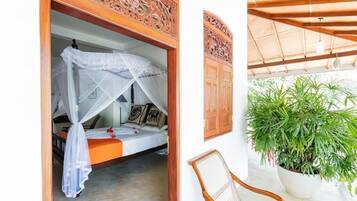 Una habitación con una cama bajo un dosel, una silla y una planta en maceta.