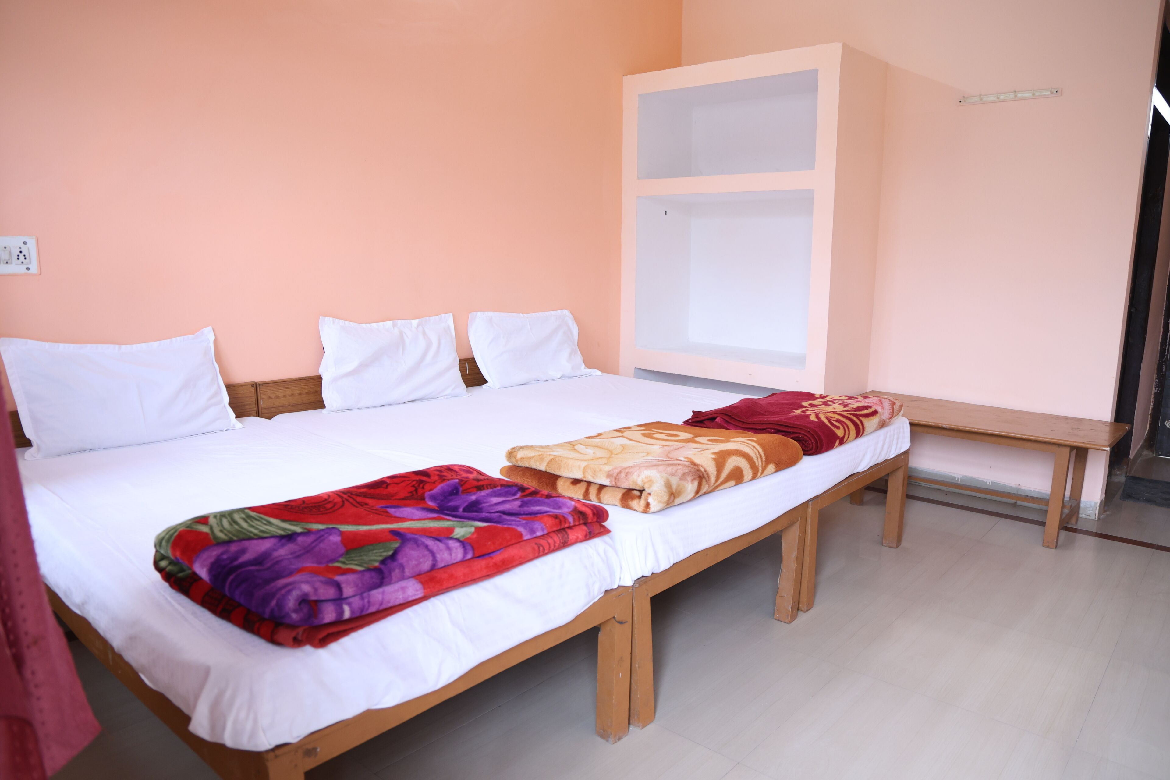 Habitación individual con cama de madera, ropa de cama blanca y una manta colorida.