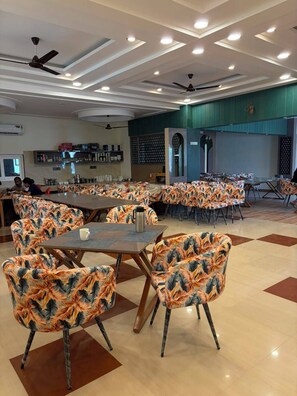 A dining area with multiple tables and chairs, ceiling fans, recessed lighting, and a kitchen area in the background. - Shree Krishna Hotel & Restaurant (Sakrai)