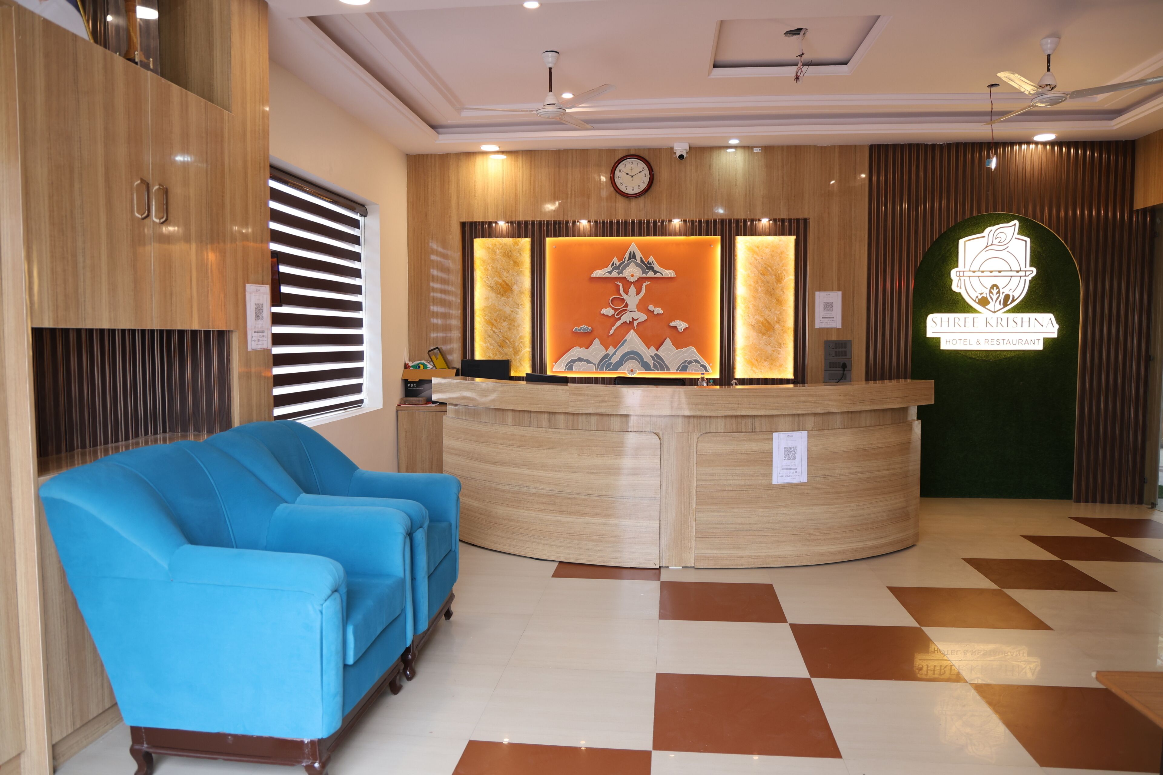 A hotel reception area with a reception desk, a blue sofa, and a clock on the wall.