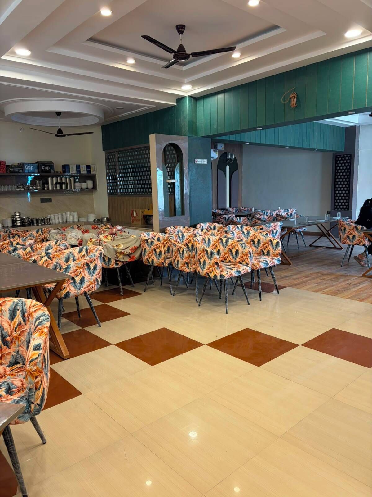 A restaurant with a checkered floor, patterned chairs, and a ceiling fan.