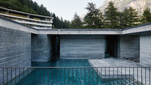 A modern building with a pool, surrounded by trees and mountains.