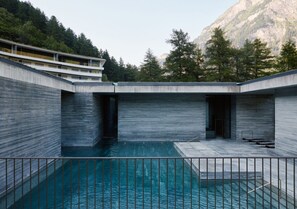Un edificio moderno con piscina, rodeado de árboles y montañas.
