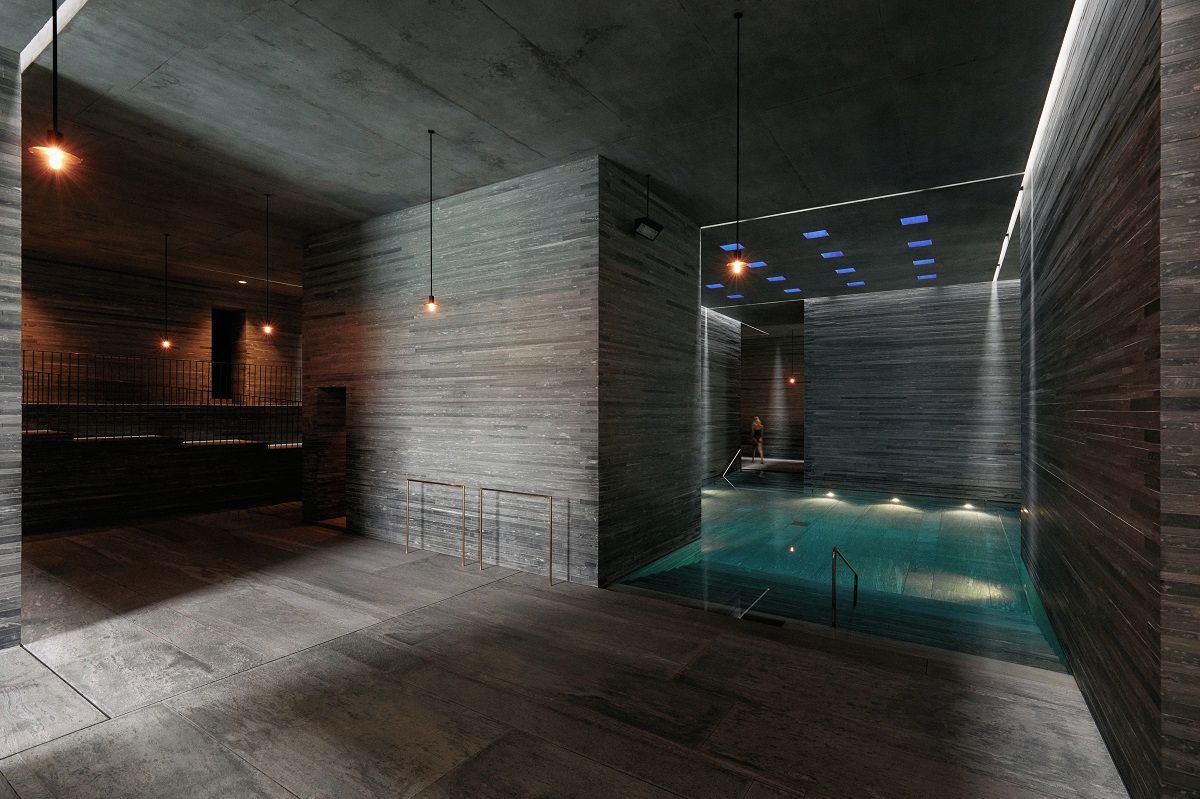 Ein moderner, überdachter Schwimmbereich mit minimalistischem Design, inklusive einer Betonwand und einem gläsernen Bereich.