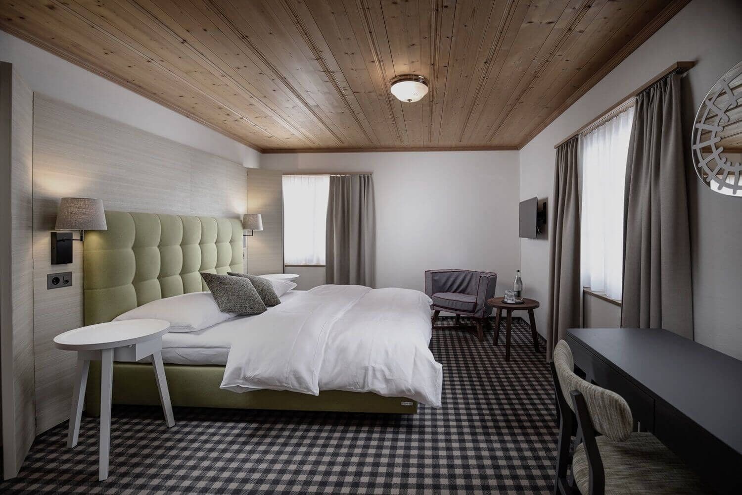 A hotel room with a bed, a small table, a chair, and a desk.