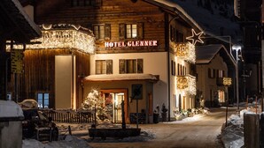 Un hotel con fachada de madera, un letrero que dice 'HOTEL GLENNER' y una calle cubierta de nieve.