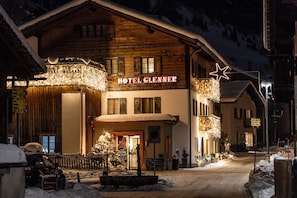 A hotel with a wooden facade, a sign reading 'HOTEL GLENNER,' and a snow-covered street.