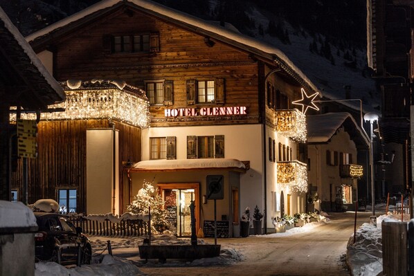 A hotel with a wooden facade, a sign reading 'HOTEL GLENNER,' and a snow-covered street.