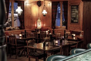 A restaurant interior with wooden paneling, multiple tables, chairs, and hanging light fixtures.