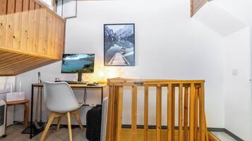 A room with a wooden desk, a computer, a chair, a bed with a wooden frame, a window, and a wall-mounted picture.