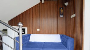 A room with a blue sofa, a wooden slatted wall, a white ceiling, and a metal railing. - Collection O Thiruparankundram City (Madurai)