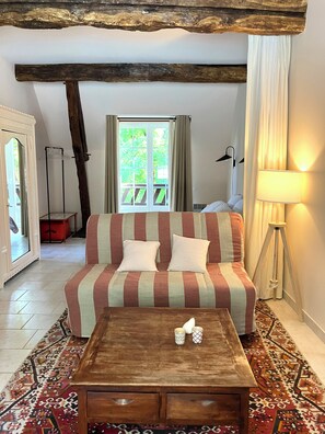 Ein Zimmer mit einer gestreiften Couch, einem Holztisch, einem gemusterten Teppich und einem großen Fenster mit Vorhängen.