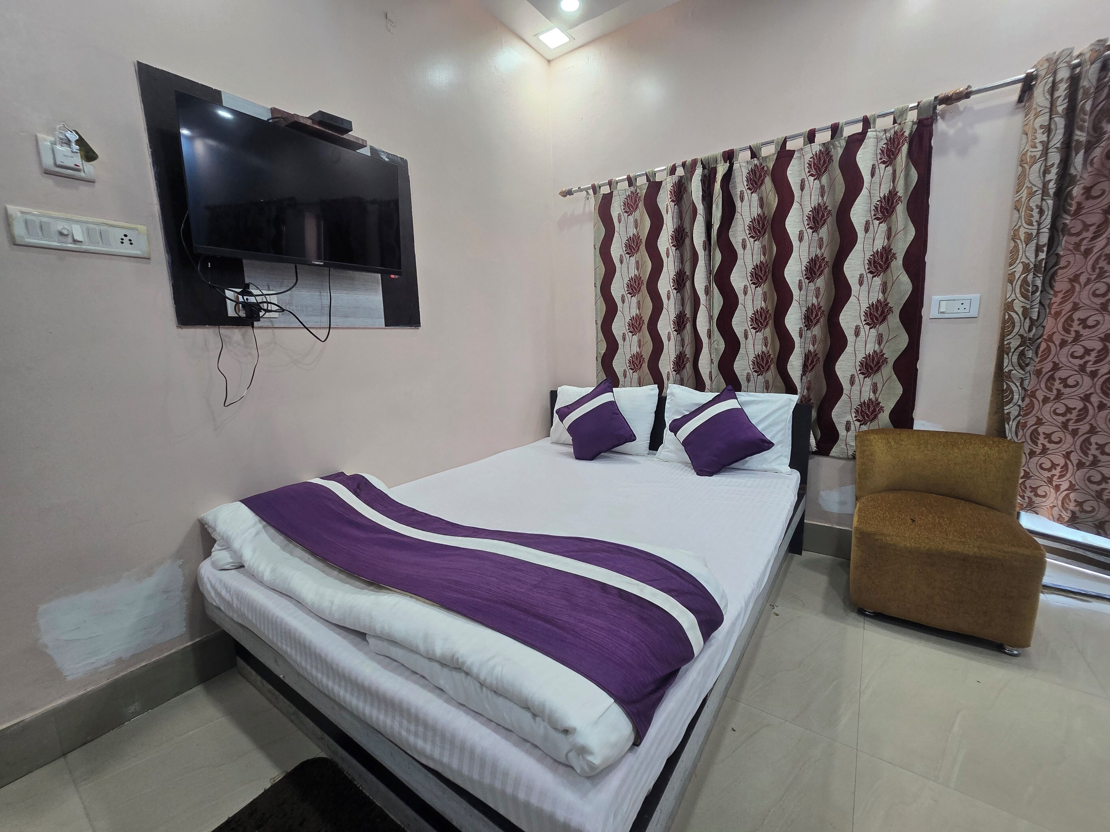 A hotel room with a bed, a television mounted on the wall, a chair, and curtains.
