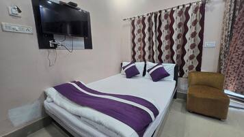 A hotel room with a bed, a television mounted on the wall, a chair, and curtains.