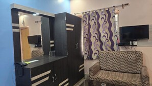 Una habitación con sofá, televisión montada en la pared, mueble con espejo y cortina estampada.