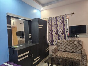 Una habitación con sofá, televisión montada en la pared, mueble con espejo y cortina estampada.